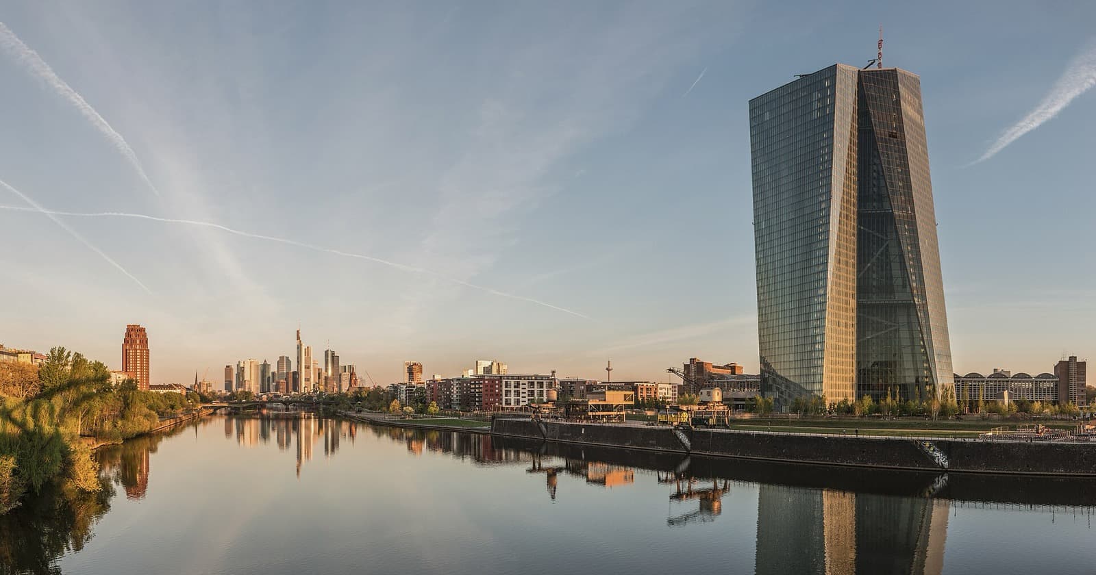 Il grattacielo della Banca centrale europea a Francoforte all'alba, con il fiume Meno in primo piano e lo skyline finanziario sullo sfondo