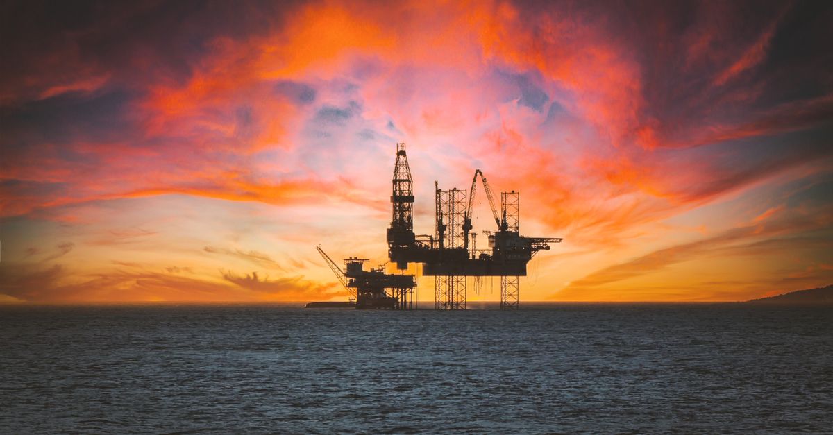 Piattaforma petrolifera al tramonto con un grafico di borsa sovrapposto, a simboleggiare l'interconnessione tra geopolitica e mercati